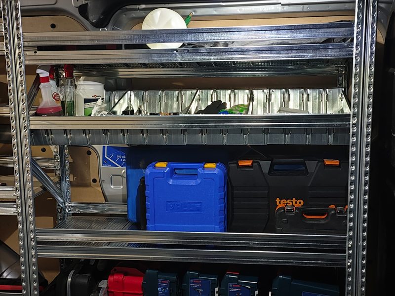 Mallettes à outils et consommables rangés sur des étagères métalliques dans une camionnette.